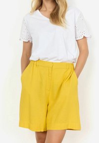Biała bawełniana koszulka z koronkowymi rękawami oraz żółte lniane szorty z bocznymi kieszeniami, prostym przodem i luźnym krojem.