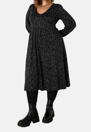Donna che indossa un vestito midi nero e grigio scuro con stampa animalier, maniche lunghe, leggings neri, stivaletti neri robusti e una collana a catena d'argento.