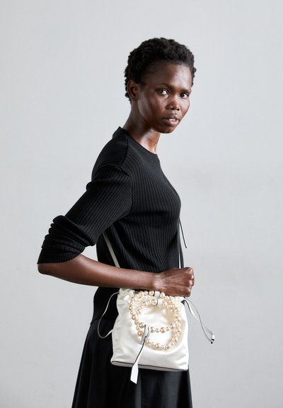 White satin drawstring bag with a pearl accent, featuring a smooth texture and side straps, paired with a fitted black ribbed sweater.