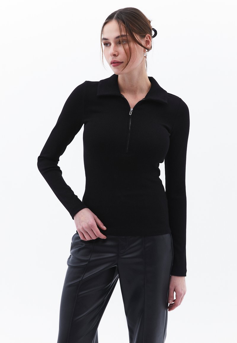 Mustapaita, jossa on pitkä hiha ja vetoketjukaulus, ribbitekstuurilla, tiukka muotoilu. Yhdistetty mustiin kiiltäviin housuihin. Yksinkertainen ja moderni ulkonäkö.