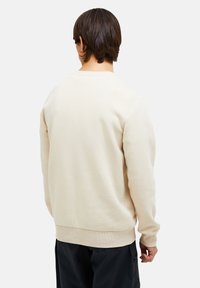 Felpa beige con collo girocollo, maniche lunghe e polsini a coste. Tessuto liscio con vita aderente. Design semplice e minimale.