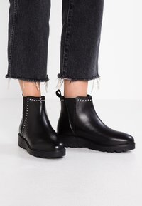 Botas de tobillo de cuero negro con una textura suave, que presentan acentos de tachuelas plateadas, laterales elásticos y una suela duradera con estrías.