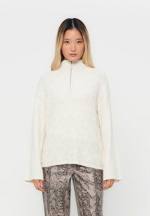 Strikket hvid pullover med høj krave og sølv lynlås. Har struktureret mønster. Sammen med tætsiddende bukser i slangeskindsdesign.