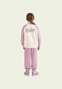 Pantaloni della tuta rosa chiaro e giacca crema e rosa con colletto bianco, con una grafica "Peanuts" sul retro.