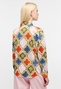Flot blouse i flere farver med et geometrisk mønster i orange, blå, grøn og pink. Fremstillet af glat stof med krave og lange ærmer.
