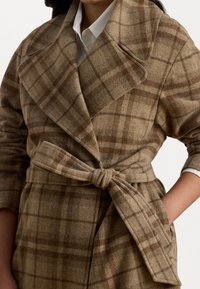 Cappotto a quadri marrone realizzato in tessuto morbido con un design avvolgente, ampi rever e vita elasticizzata. Presenta una finitura testurizzata e due tasche anteriori.