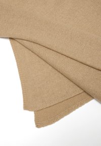 Tessuto a maglia beige, morbido al tatto, piegato con una finitura liscia, caratterizzato da un bordo pulito. Colore marrone chiaro con un motivo di maglia uniforme.