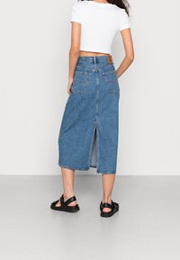 Jeanskjol med rak silhuett, ljusblå färg, längd till mitten av vaden, med en slits bak, två bakfickor och en läderetikett.