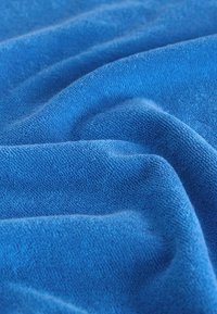 Zbliżenie miękkiej, teksturowanej niebieskiej tkaniny z widocznymi tkanymi pętlami tworzącymi delikatne fałdy i cienie.