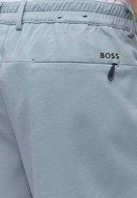 Pantalon gris clair avec taille élastique et poche arrière zippée avec le mot BOSS imprimé au-dessus de la poche.