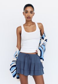Vit ribbad linne, grå lager-på-lager volangkjol och en flerfärgad randig stickad cardigan. Outfiten har en avslappnad, lätt design.