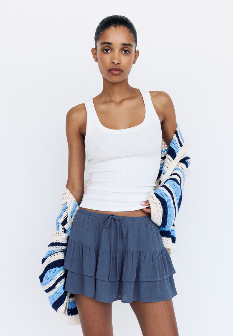 Vit ribbad linne, grå lager-på-lager volangkjol och en flerfärgad randig stickad cardigan. Outfiten har en avslappnad, lätt design.