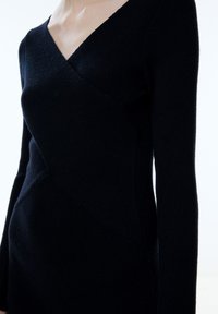 Schwarzes Strickkleid mit figurbetonter Silhouette, langen Ärmeln und einem tiefen V-Ausschnitt mit einem sich überkreuzenden diagonalen Nahtmuster.