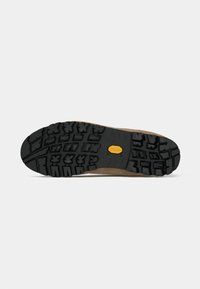 Brauner Wanderschuh mit tiefem, schwarzem Gummiprofil und gelbem Vibram-Logo in der Mitte, vor einem weißen Hintergrund.
