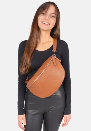 Young woman wearing black long-sleeve top and leather pants, smiling, with large brown leather crossbody bag across chest.