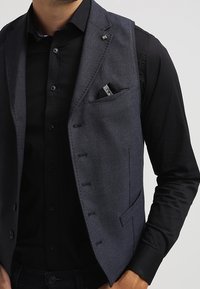 Mörkgrå väst med en texturerad yta, försedd med en enkel bröstficka, sex knappstängningar och en slät krage.