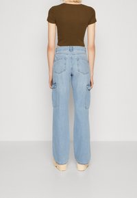 Pantalones cargo de mezclilla azul claro con piernas anchas, que cuentan con bolsillos traseros y bolsillos laterales. Combinados con una blusa ajustada de manga corta marrón.