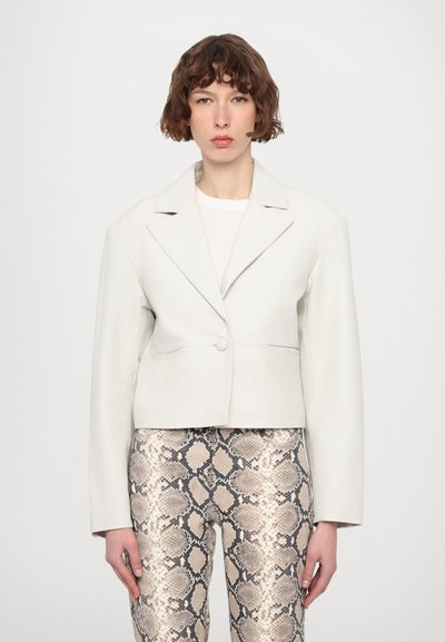 Kürzerer weißer Lederblazer mit Reverskragen, einem Knopfverschluss und seitlichen Taschen, kombiniert mit metallisch schlangen-musternden Hosen.
