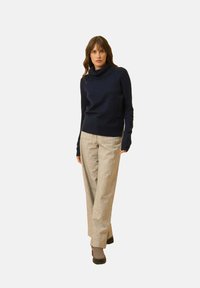 Navyblauer Rollkragenpullover aus weichem Stoff, kombiniert mit hellgrauen karierten weiten Hosen und Ankle Boots, die ein schlichtes Design aufweisen.