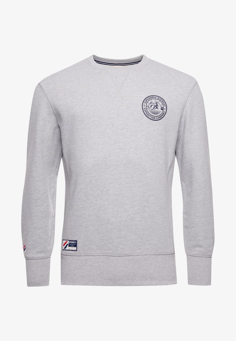 Sweat-shirt gris clair à col rond avec logo montagne sur la poitrine et petite étiquette de marque près de l'ourlet et du poignet de la manche.