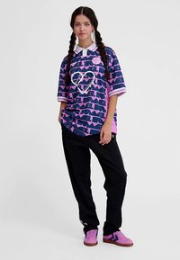 Lila och blå grafisk skjorta med texten "LEVEL", vit hjärtdesign, tillsammans med svarta byxor och rosa sneakers med svarta detaljer.