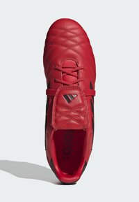 Scarpa da calcio rossa in pelle con superficie testurizzata, caratterizzata da una punta arrotondata, accenti neri e lacci. Include una linguetta imbottita.