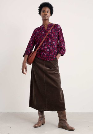 Blouse à imprimé floral multicolore avec fermeture à boutons, associée à une longue jupe en velours côtelé marron. Portée avec des bottes en cuir marron hauteur genou et un sac bandoulière.