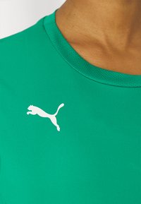 Zelena sportska majica izrađena od mekog materijala; ima teksturirani ovratnik i bijeli Puma logo na prsima.