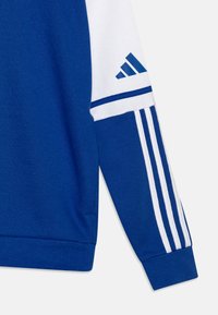 Sweatshirt bleu avec des manches blanches. Présente trois rayures blanches le long des manches et un logo Adidas en bleu. Tissu doux, design à col ras-du-cou.