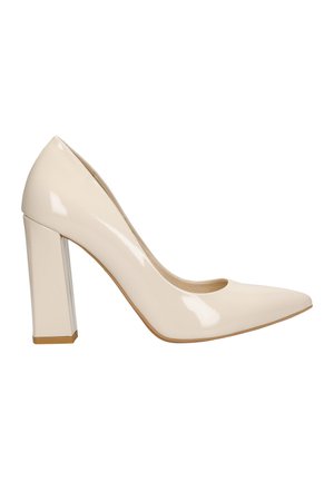 Escarpin à talon haut en cuir verni beige avec un bout pointu et un talon bloc, présentant une finition brillante et un design ajouré sur les côtés.