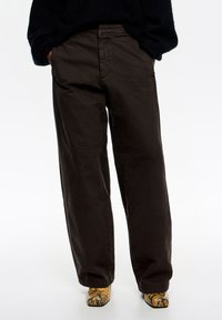 Pantalones de algodón oscuros de corte amplio y ajuste relajado, con detalles de costura sutiles, combinados con calzado amarillo y negro de estampado.