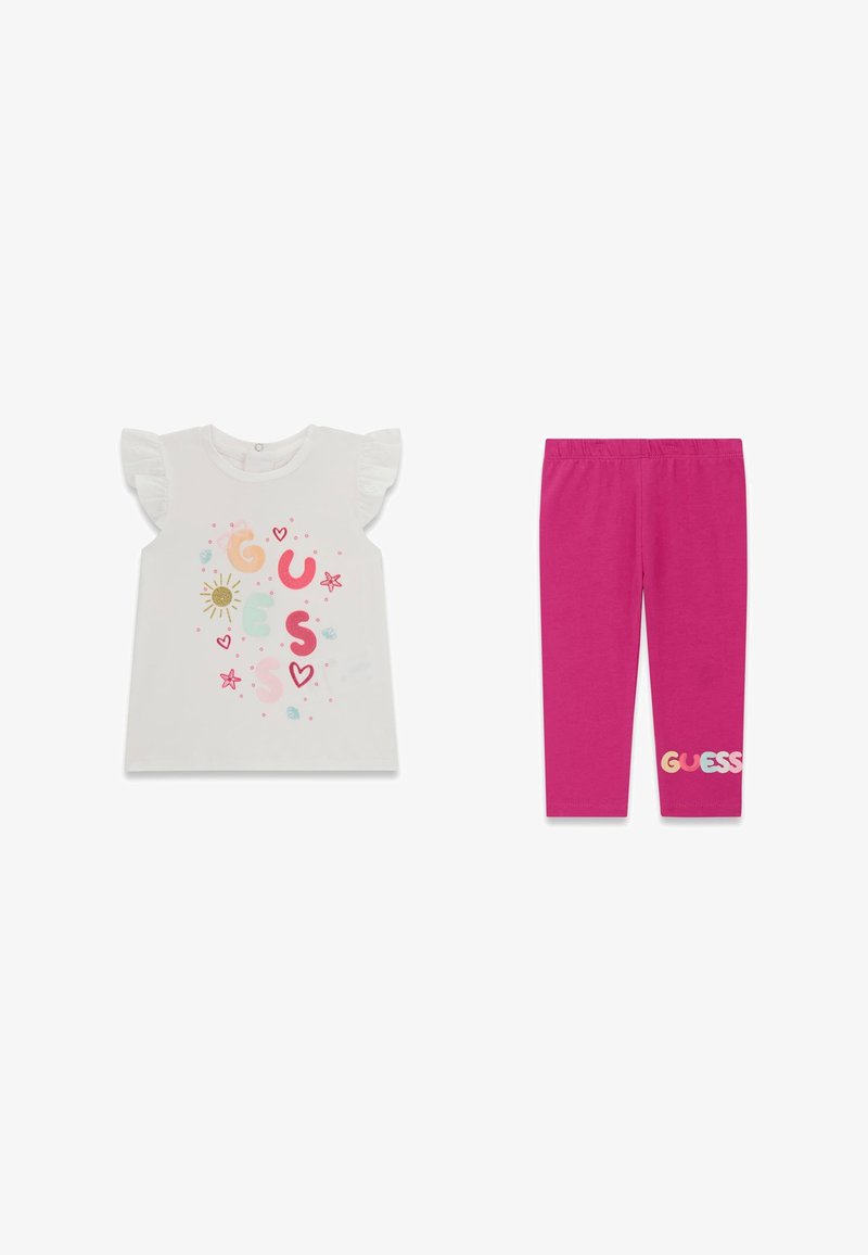 T-shirt blanc à manches volantées pour tout-petit avec logo coloré "GUESS" et soleil, associé à des leggings rose vif avec texte "GUESS" près de l'ourlet.