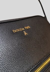 Borsa a mano in pelle nera con superficie testurizzata, logo dorato "PATRIZIA PEPE" e dettaglio con zip dorata lungo il lato.
