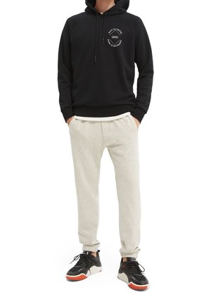 Sudadera negra con capucha y logo gráfico, combinada con pantalones jogger grises claros. Calzado negro con detalles rojos y blancos.