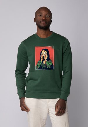 Grüne Sweatshirt mit Grafik einer Person mit weit aufgerissenen Augen und Händen im Gesicht, vor einem roten Hintergrund. Weiche Textur.