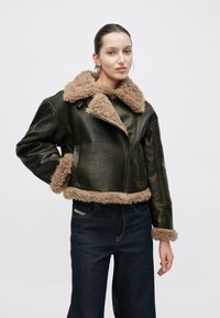 Giacca in pelle marrone con colletto e polsini in ecopelliccia beige. Presenta una zip frontale e tasche laterali, con un design corto.