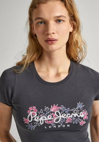 Camiseta gris ajustada de manga corta, con un diseño floral en tonos rosa y azul, y el texto "Pepe Jeans London" en blanco.