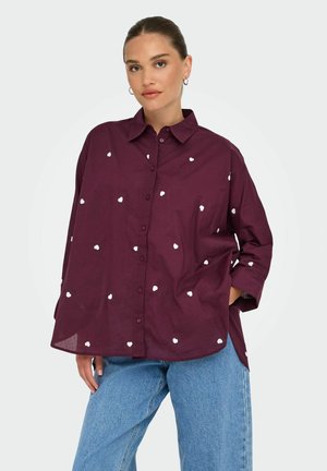 Bordeaux knap-up skjorte med hvide hjerte-mønstre, der har en afslappet pasform og en kravehals, parret med blå jeans.