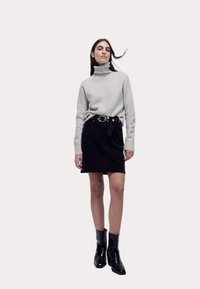 Maglione a collo alto grigio chiaro, gonna nera con cintura e stivaletti neri lucidi. Progettato per una vestibilità moderna con texture morbide.