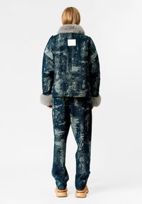 Conjunto de chaqueta y pantalón de denim en azul oscuro con un patrón texturizado; la chaqueta presenta un cuello de piel gris y puños a juego.