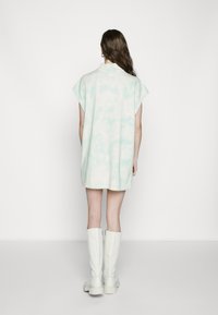 Short-sleeve, oversized dress in light mint tie-dye pattern, made of soft fabric, with a curved hem and no visible fastenings, worn with tall white boots.
