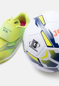 Παιδικό ποδοσφαιρικό παπούτσι σε κίτρινο και πράσινο δίπλα σε μια λευκή ποδοσφαιρική μπάλα μεγέθους 3 με μπλε και κίτρινα γεωμετρικά σχέδια.