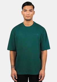 Dunkelgrünes, übergroßes T-Shirt aus Baumwollmischung, mit kurzen Ärmeln und einem dezenten "DROPSIZE"-Logo auf der Vorderseite.