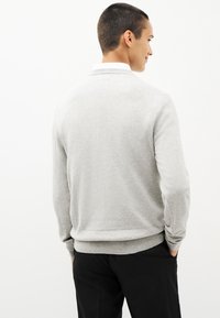 Pull en coton gris avec des poignets et un ourlet côtelés, présentant un design classique à encolure ras du cou et une finition douce et sans texture.