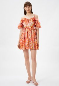 Blommig klänning i nyanser av rosa och orange, tillverkad av lättviktig tyg. Har off-shoulder volanger och en flerlagerskjol.