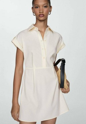 Robe à manches courtes, avec col, en tissu crème clair, dotée d'une fermeture à boutons sur le devant et d'une taille cintrée, associée à un sac en osier tan muni de anses noires.