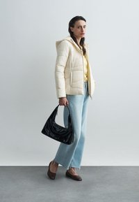 Kremowa kurtka puchowa z kapturem, żółta bluzka, jasnoniebieskie spodnie z szerokimi nogawkami, brązowe buty i czarna torebka. Gładkie faktury na całej powierzchni.