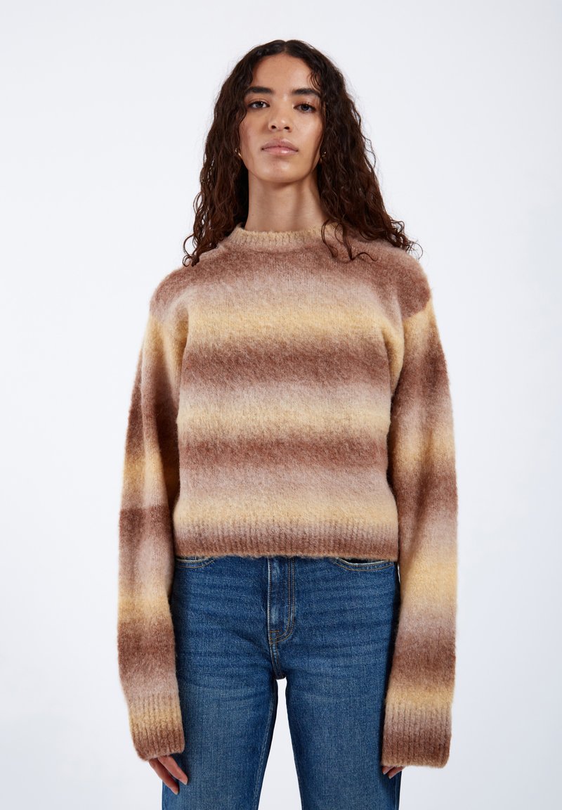 Braun- und gelbgestreifter Pullover aus weichem Strickmaterial mit Rundhalsausschnitt und langen, lockeren Ärmeln, kombiniert mit blauen Jeans.