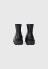 Bottines noires avec une texture lisse, des côtés légèrement nervurés, des bouts ronds et des semelles épaisses en caoutchouc avec un motif de traction.