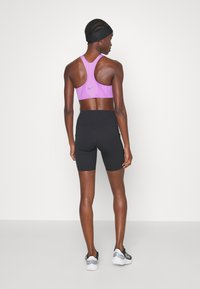 Soutien-gorge de sport athlétique violet avec un design texturé, associé à un short noir taille haute. Modèle portant un bandeau noir et des chaussures de sport.